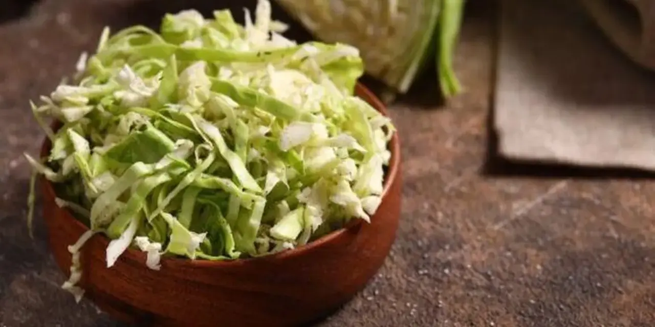 Fein geschnittener Spitzkohl in einer Holzschale, bereit, in der Pfanne gebraten zu werden. Ein halber Spitzkohl liegt im Hintergrund.