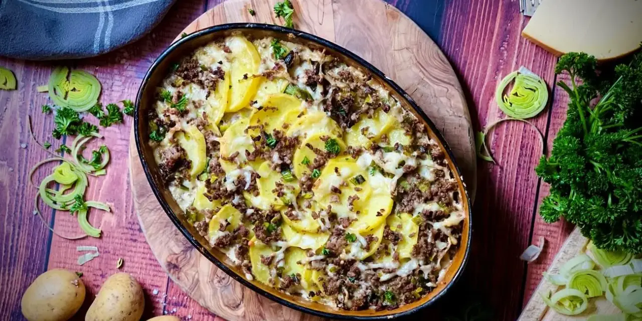 Herzhafter kartoffelauflauf mit hackfleisch, überbacken mit Käse und garniert mit Petersilie. Dazu frische Kartoffeln, Lauch und ein Stück Käse.