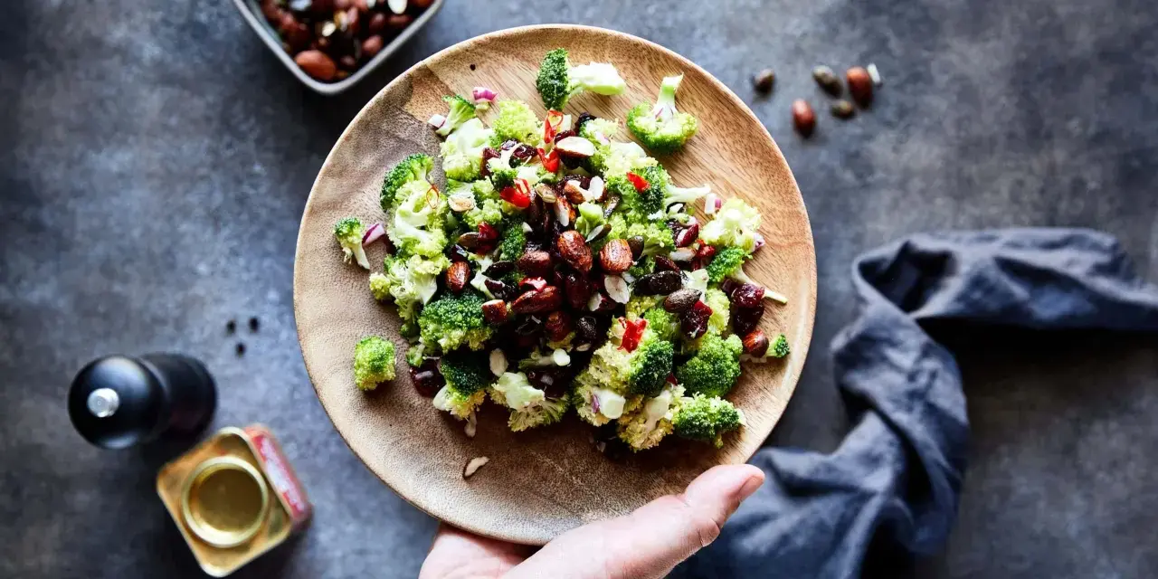 Frischer Brokkoli Salat mit Nüssen und roten Zwiebeln auf einem Holzteller, bereit zum Genießen.