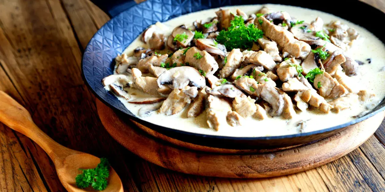 Putengeschnetzeltes mit Pilzen in cremiger Soße, garniert mit Petersilie, serviert in einer Pfanne auf rustikalem Holztisch.