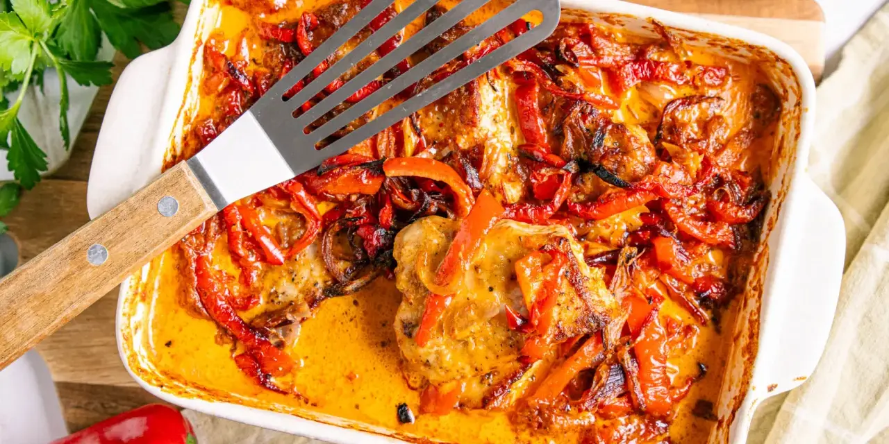 Herzhaftes Paprika Sahne Schnitzel in einer Auflaufform, mit roten Paprikastreifen und Zwiebeln in cremiger Sauce.