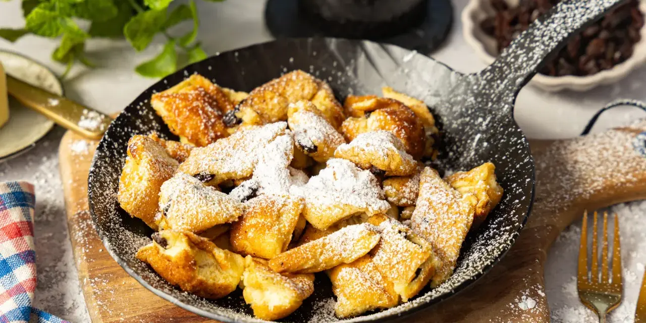 Ein fluffiger Kaiserschmarrn im Pfännchen, bestäubt mit Puderzucker. Perfekt für ein süßes Frühstück oder Dessert.