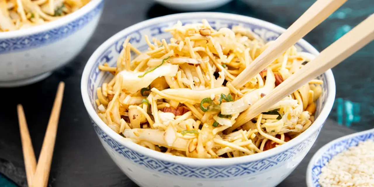 Ein Schüsselchen mit friss dich dumm Salat, Nudeln, Gemüse und Erdnüssen, bereit zum Genießen mit Stäbchen.