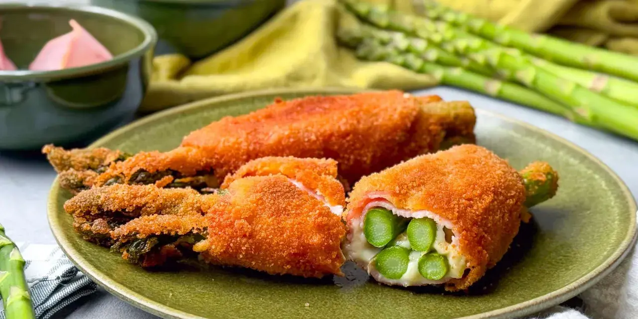 Knusprig paniertes Spargel Cordon Bleu mit Schinken und Käse gefüllt, auf einem grünen Teller angerichtet.