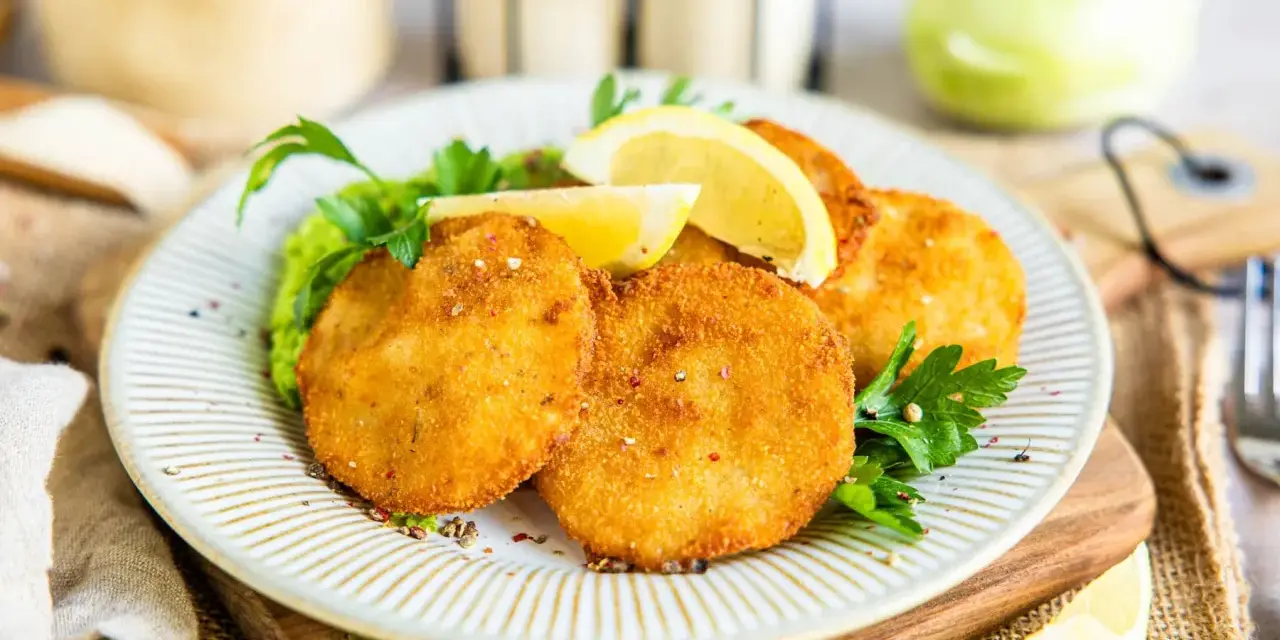 Knuspriges Kohlrabi Schnitzel auf einem Teller mit Erbsenpüree, Zitrone und Petersilie. Ein Genuss für Vegetarier!