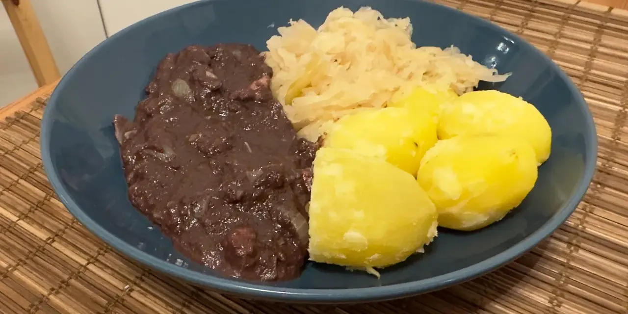 Ein Teller mit deftigem Essen: dunkle Soße, Sauerkraut und Salzkartoffeln. Erinnert an die gute, alte tote Oma.