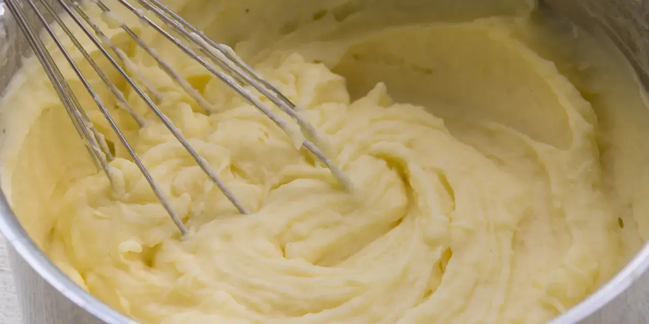 Cremiger kartoffelbrei ohne butter wird mit einem Schneebesen in einem Topf zubereitet.