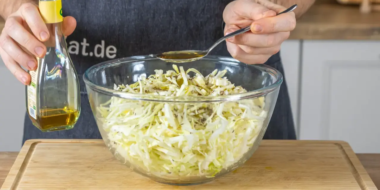 Ein Löffel Öl wird über den fein geschnittenen Spitzkohl gegeben, der für Omas Spitzkohlsalat vorbereitet wird.