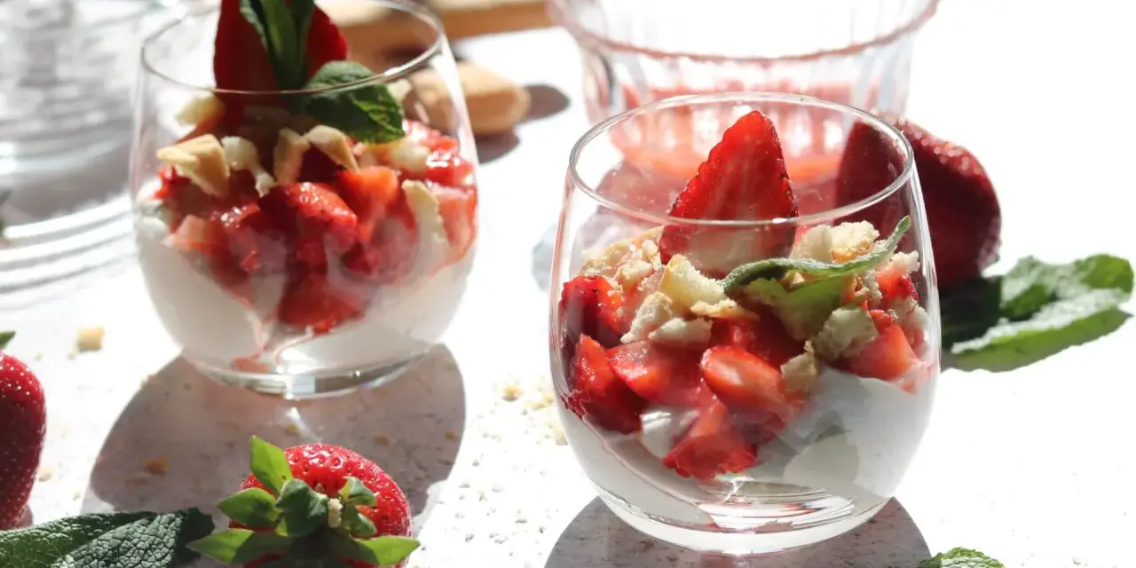 Zwei Gläser mit einem leichten Erdbeer Quark Dessert, garniert mit frischen Erdbeeren und Minze.