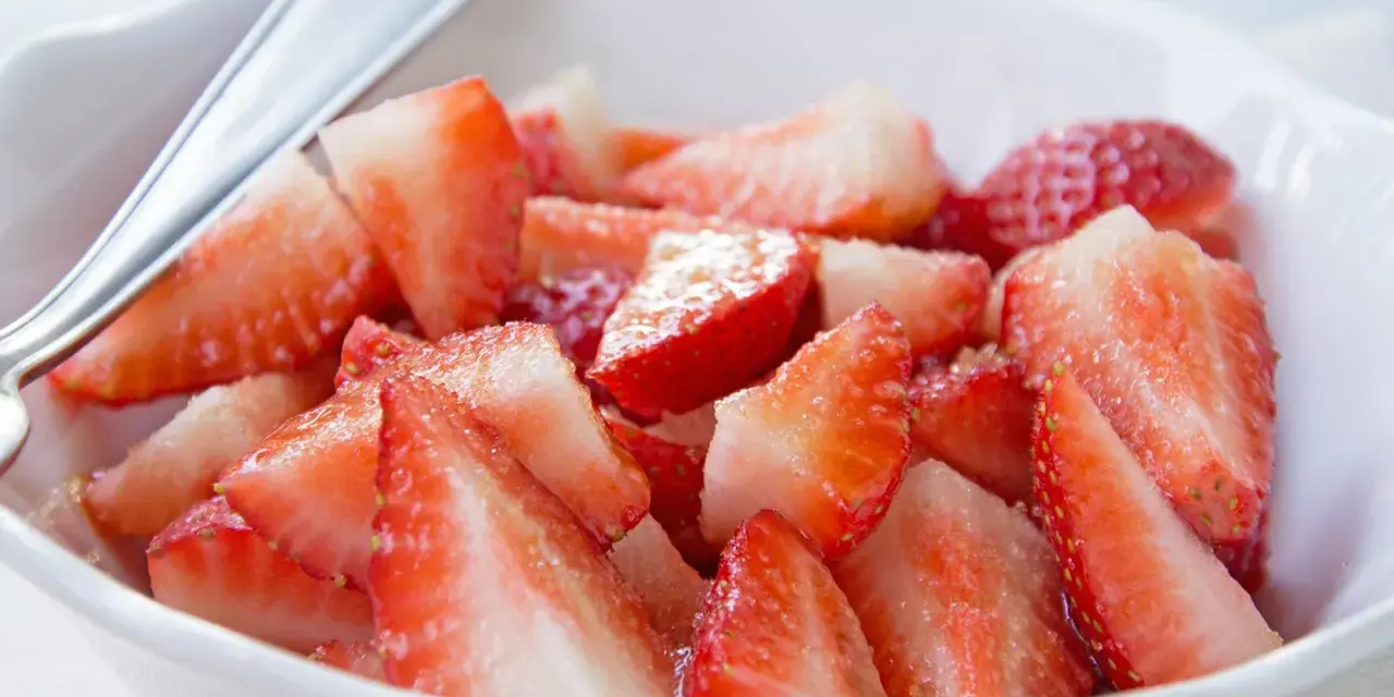 Schüssel mit marinierten Erdbeeren, die mit einem Löffel serviert werden. Saftige, rote Erdbeerstücke glänzen im Licht.