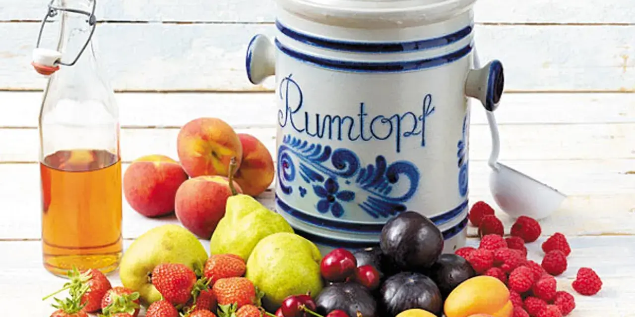Früchte für ein Rumtopf Rezept nach Oma: Erdbeeren, Kirschen, Aprikosen, Pflaumen, Pfirsiche, Birnen, Himbeeren und eine Flasche Schnaps.