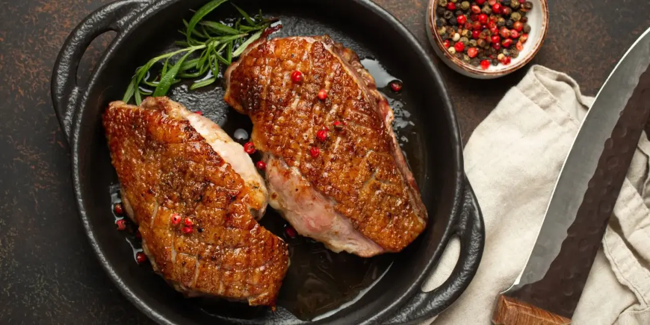 Zwei perfekt gebratene Entenbrüste in einer Pfanne, garniert mit Rosmarin und rosa Pfeffer. Ein klassisches Entenbrust Rezept, bereit zum Servieren.