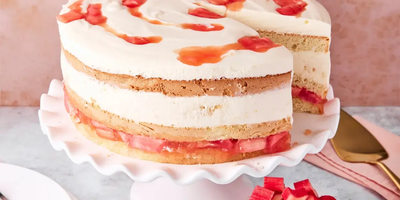 Eine köstliche Erdbeer Rhabarber Torte mit Sahne und Fruchtstücken, auf einem rosa Tortenständer präsentiert.