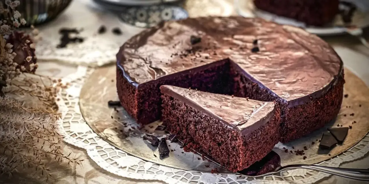 Ein saftiger Schokoladenkuchen mit glänzender Glasur, ein Stück wurde herausgeschnitten. Der einfache Kuchenteig sieht köstlich aus.