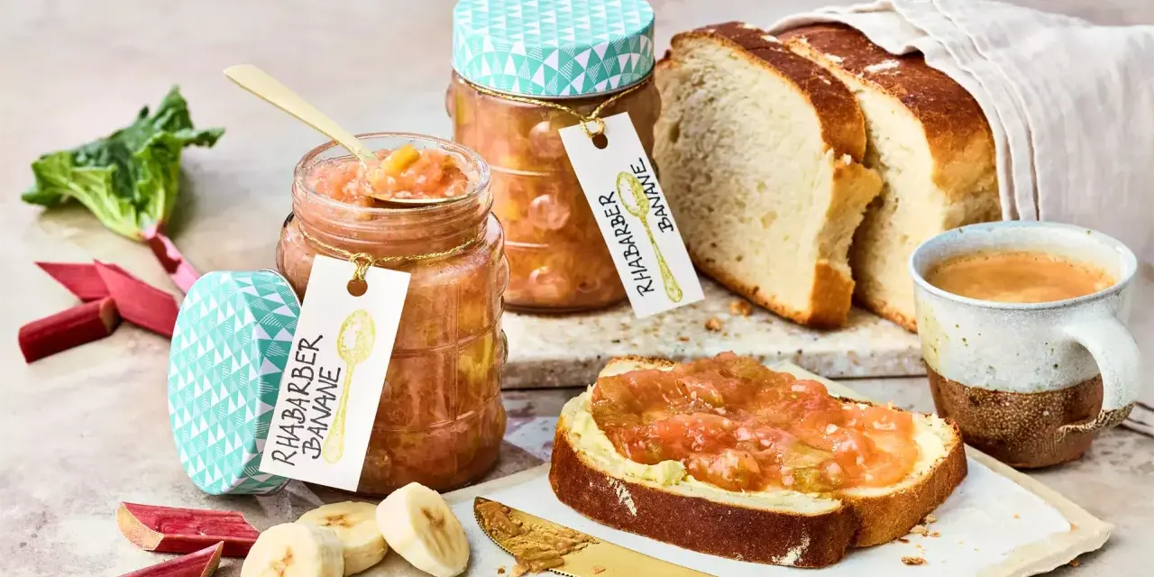 Zwei Gläser Rhabarber Bananen Marmelade, frischer Rhabarber, Bananenscheiben, Brot und Kaffee.