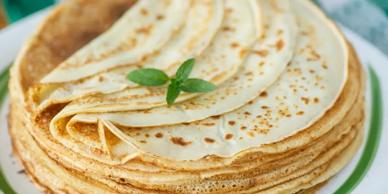 Ein Stapel goldbrauner Pfannkuchen, wie nach Omas Pfannkuchen Rezept gemacht, mit einem Minzblatt garniert.