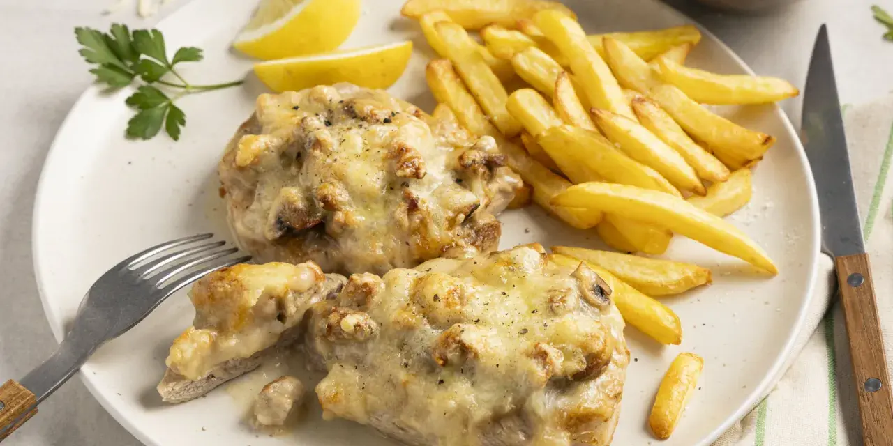 Zwei saftige Steak au Four mit geschmolzenem Käse, dazu knusprige Pommes Frites, Zitronenspalten und ein kleiner Salat.