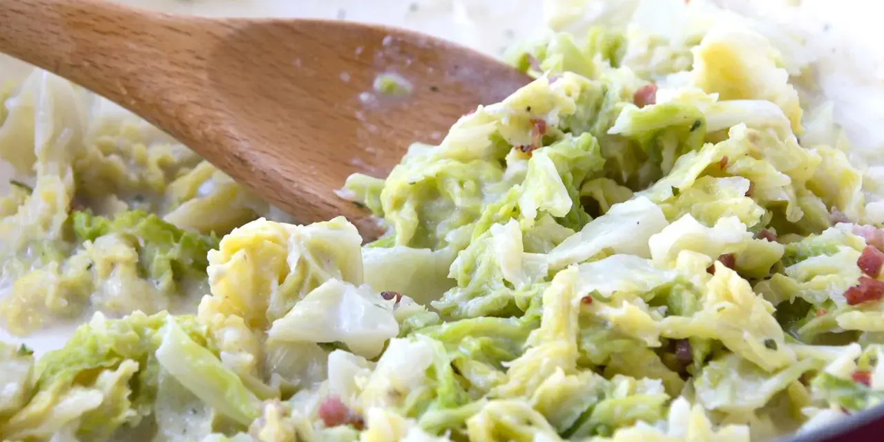 Cremiger Wirsing mit Speck, zubereitet mit einem Holzlöffel. Ein leckeres Gericht, das Lust auf mehr wirsing rezepte macht.