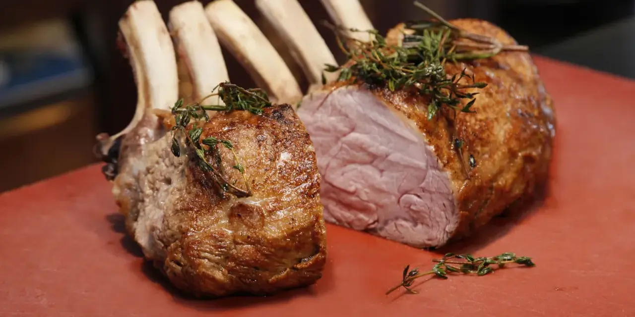 Ein gebratener Semerrolle Kalb mit Kräutern auf rotem Untergrund.