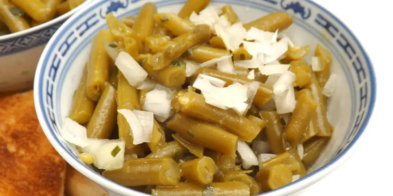 Bohnensalat rezept: Grüne Bohnen mit Zwiebeln in einer Schüssel, daneben geröstetes Brot.