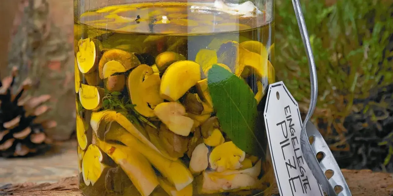 Glas mit eingelegten Pilzen, Kräutern und Lorbeerblatt. Ein Etikett mit der Aufschrift "Eingelegte Pilze" hängt am Glas.