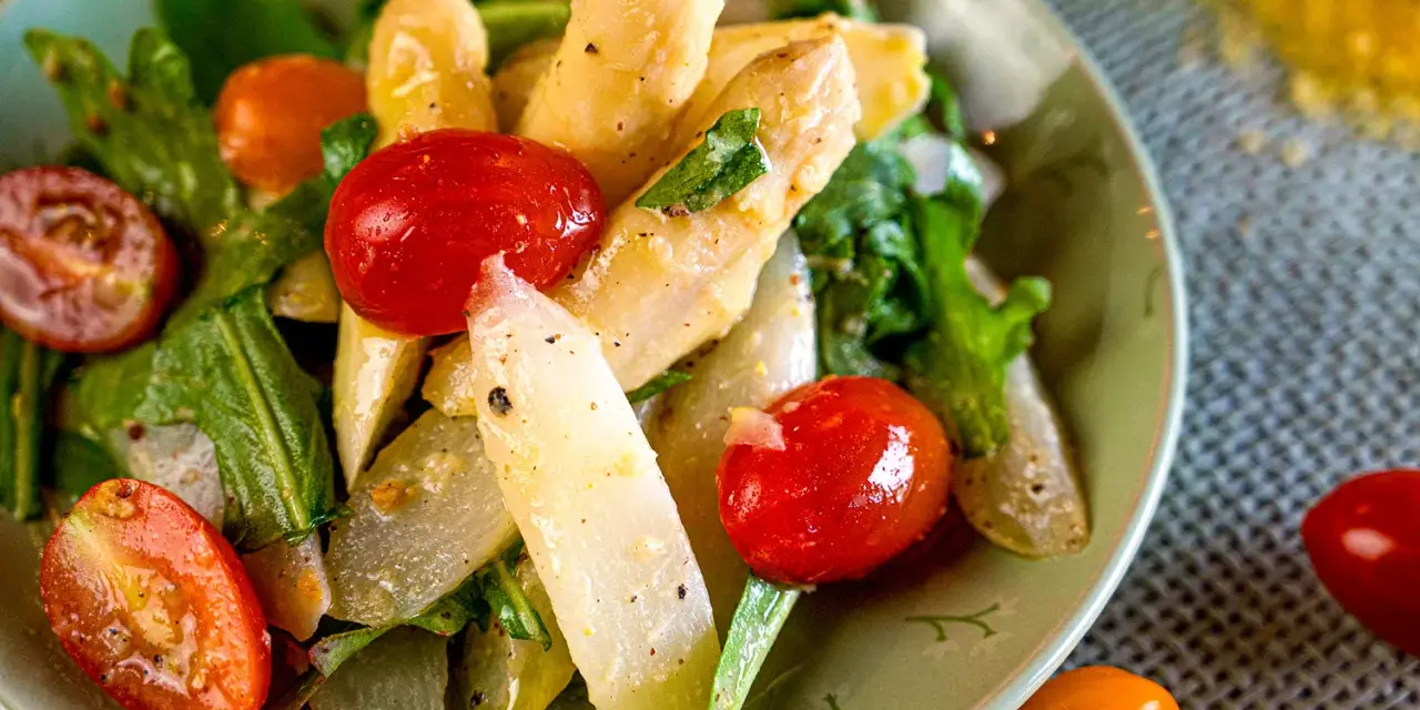 Ein Teller mit weltbestem Spargelsalat, garniert mit Kirschtomaten und frischen Kräutern. Ein Genuss für Augen und Gaumen.