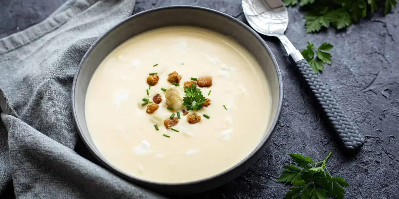 Cremige Spargelsuppe aus Schalen, garniert mit Croutons und frischen Kräutern. Ein Löffel liegt daneben.