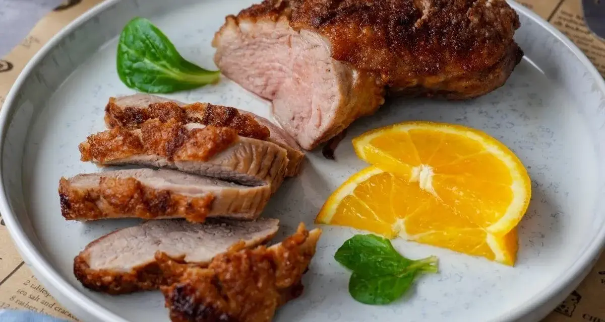 Saftige entenbrust im airfryer, perfekt gebräunt und in Scheiben geschnitten, serviert mit frischen Orangenscheiben und grünen Blättern.