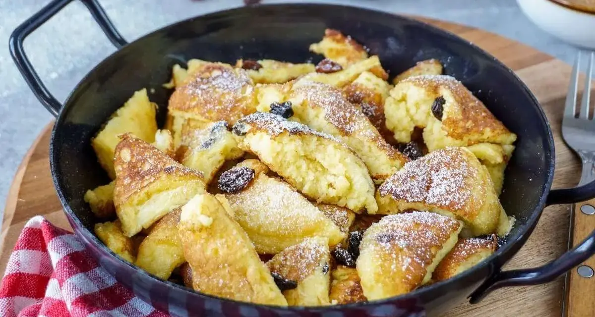 Leckerer, schneller Kaiserschmarrn im Backofen, bestäubt mit Puderzucker und Rosinen, serviert in einer Pfanne.