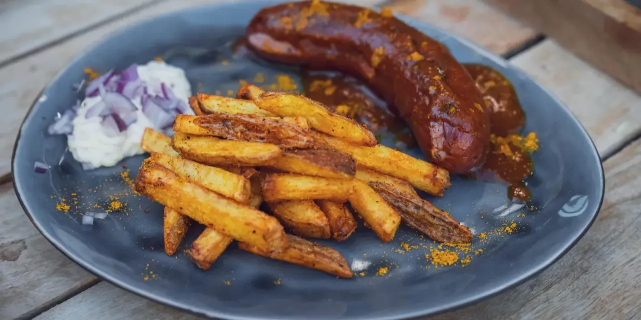 Eine saftige Currywurst im Backofen mit knusprigen Pommes und einem Klecks Mayo mit Zwiebeln.