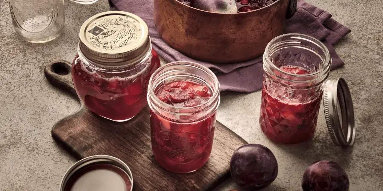Frisch eingekochte Pflaumenmarmelade im Glas, bereit für das pflaumenmarmelade rezept. Frische Pflaumen liegen daneben.