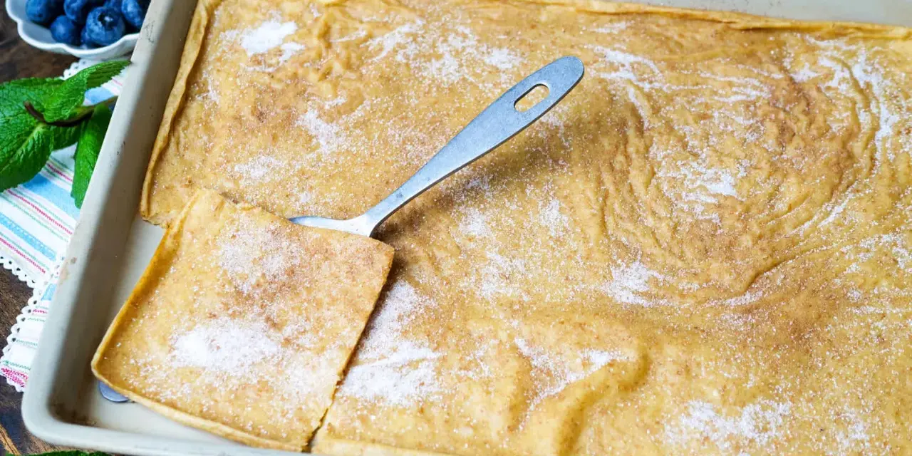 Großer, goldbrauner Ofenpfannkuchen mit Zucker und Zimt bestreut, bereit zum Servieren. Blaubeeren und Minze garnieren.