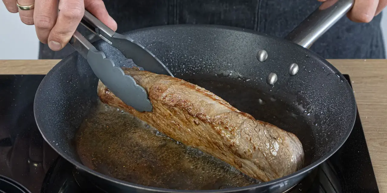 Ein saftiges Schweinefilet brät in der Pfanne. Einfache Rezepte für zartes Fleisch in der Pfanne gelingen so.