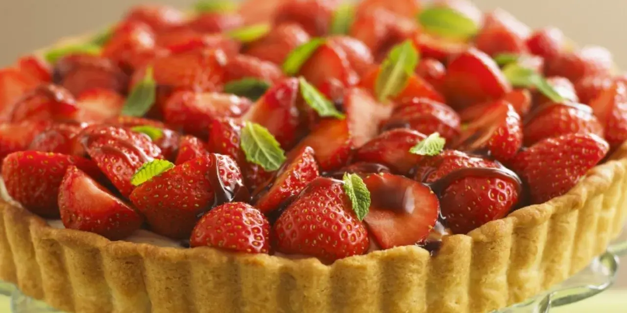 Ein köstlicher Erdbeerkuchen ohne Pudding, üppig belegt mit frischen Erdbeeren und Minze, auf einem Tortenständer.