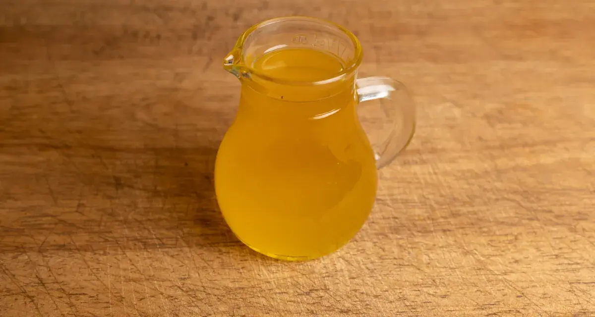 Ein kleines Glas mit goldgelbem Butterschmalz steht auf einem Holzbrett. Perfekt zum butterschmalz selber machen.
