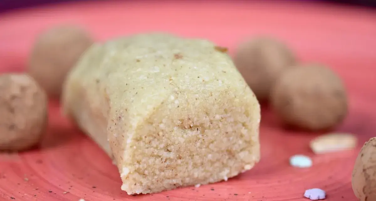Ein Block selbstgemachtes Marzipan, ohne Rosenwasser, liegt auf einer roten Platte. Daneben sind Pralinen und bunte Zuckerstreusel.