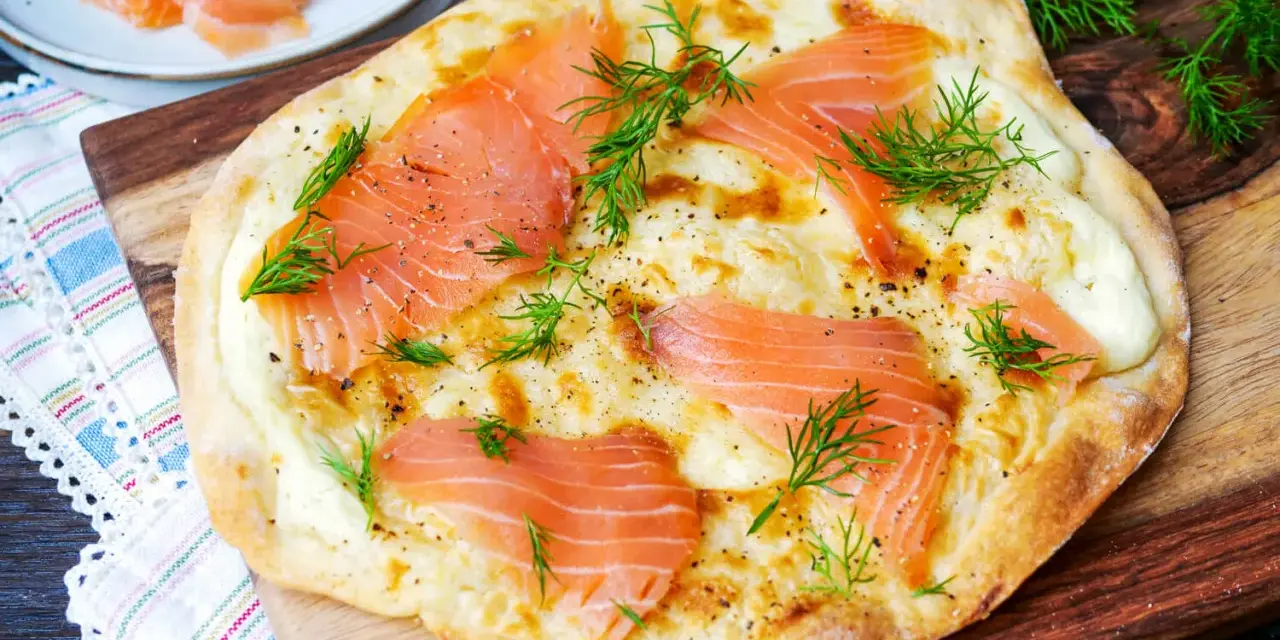 Flammkuchen mit Lachs, belegt mit zarten Lachsscheiben und frischem Dill, auf einem Holzbrett serviert.