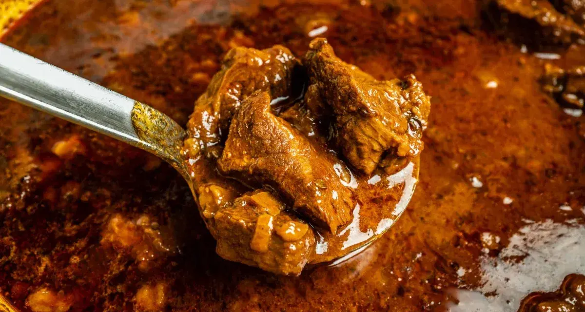 Ein Löffel voller herzhaftem Wildschweingulasch, bereit zum Servieren. Dieses Wildschweingulasch Rezept verspricht ein köstliches Gericht.