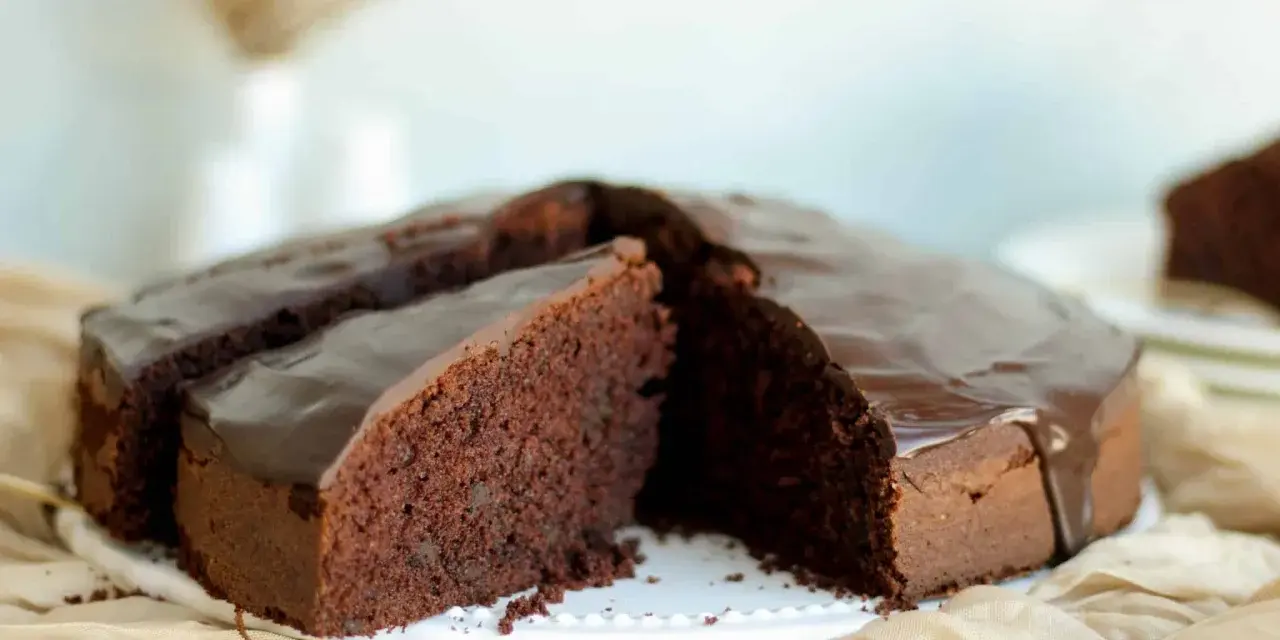 Ein saftiger Schokokuchen mit glänzender Glasur, perfekt für jedes schokokuchen rezept. Ein Stück ist bereits angeschnitten.