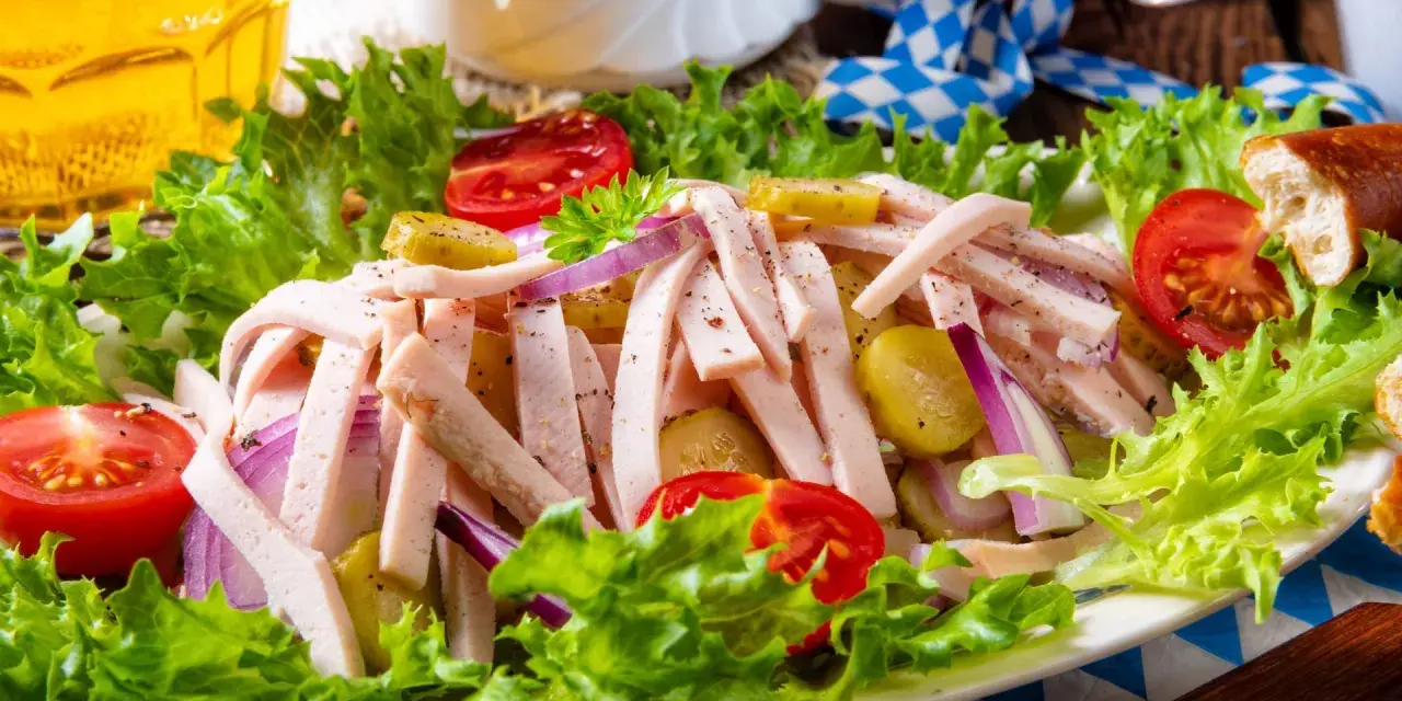 Ein leckerer Wurstsalat mit Gurken, Tomaten und Zwiebeln, garniert mit Salat. Perfekt für ein deftiges wurstsalat rezept.