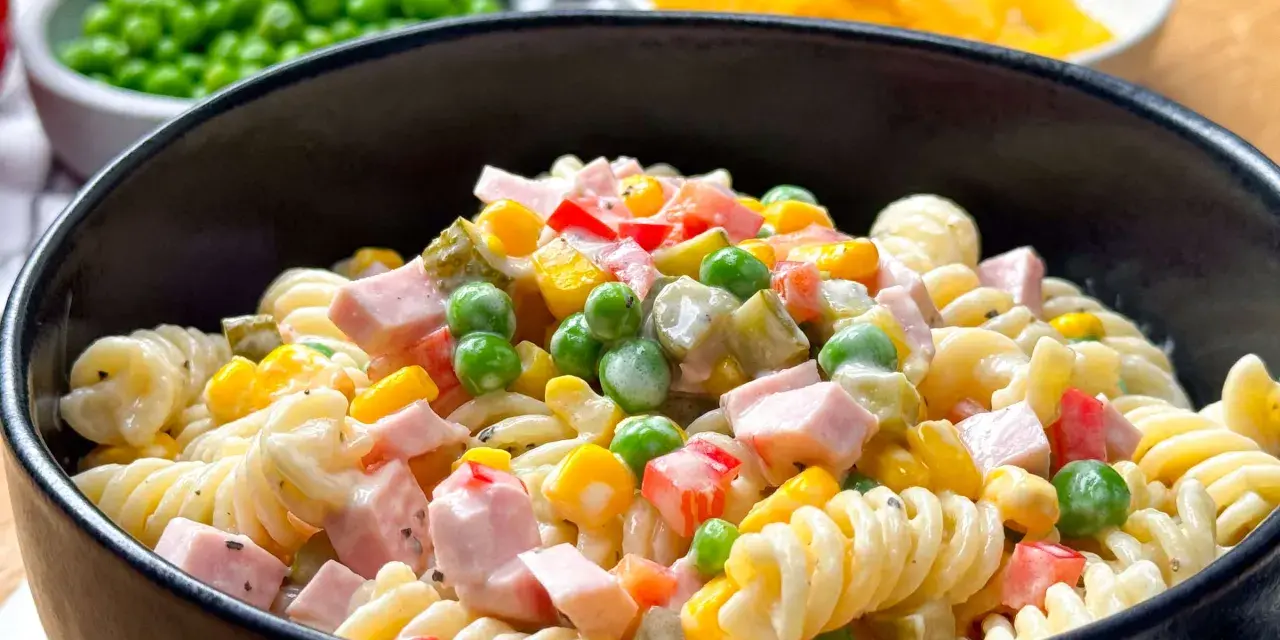 Ein cremiger nudelsalat mit mayonaise, garniert mit Erbsen, Mais, Paprika und Schinkenwürfeln.