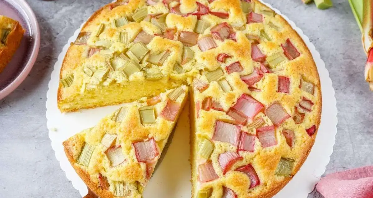 Saftiger Rhabarberkuchen, ein Klassiker unter den Rezepten mit Rhabarber. Ein Stück wird gerade herausgehoben.
