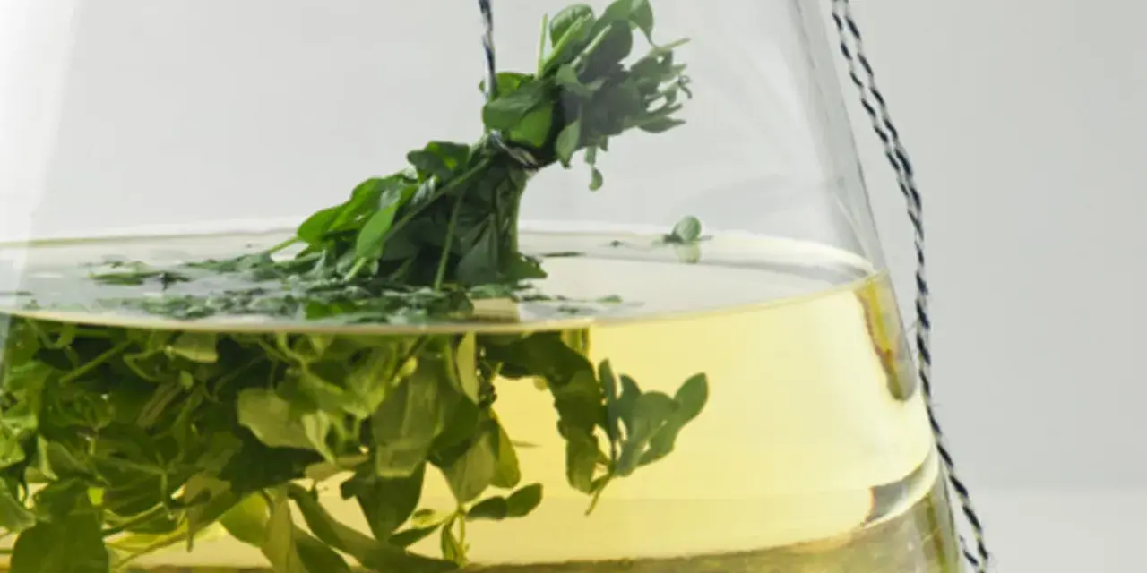 Ein Strauß frischer Waldmeister hängt in einer Glasbowle mit gelblicher Flüssigkeit. Perfekt für ein Maibowle Rezept.