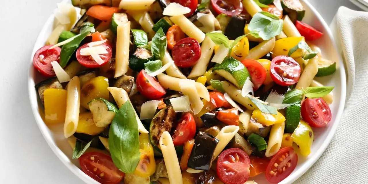 Bunter Nudelsalat ohne Mayo mit Penne, gegrilltem Gemüse, Kirschtomaten und Basilikum, garniert mit Parmesan.