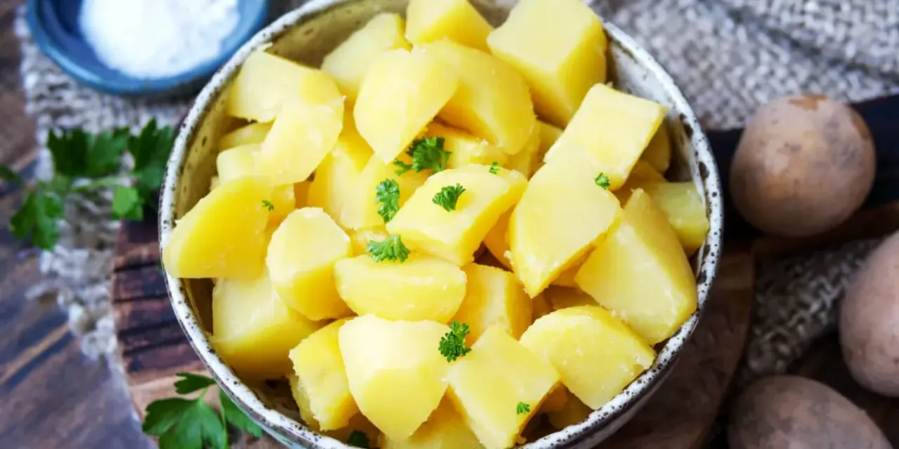 Schüssel mit dampfenden Salzkartoffeln, garniert mit Petersilie. Daneben eine kleine Schale mit Salz und rohe Kartoffeln.
