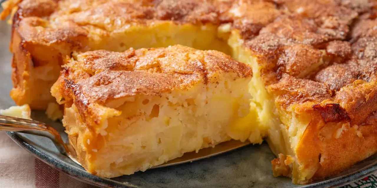 Ein Stück von einem goldbraunen, sehr feinen Apfelkuchen mit Zimt bestreut, wird mit einer Tortenheber herausgehoben.