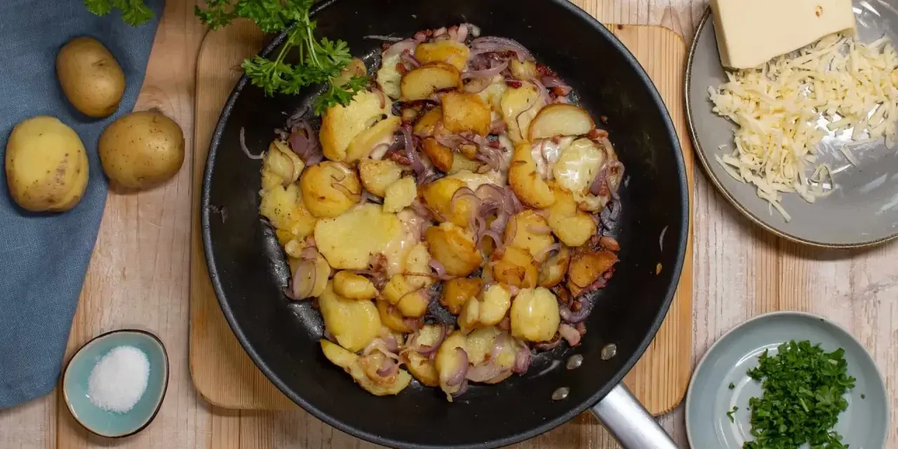Bratkartoffeln mit Zwiebeln und Käse in der Pfanne, dazu frische Petersilie und Salz.