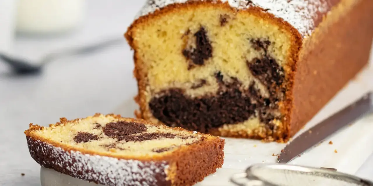 Ein saftiger marmorkuchen mit Puderzucker bestäubt, daneben ein Stück Kuchen und ein Sieb. Perfekt mit einem Klecks Sahne.