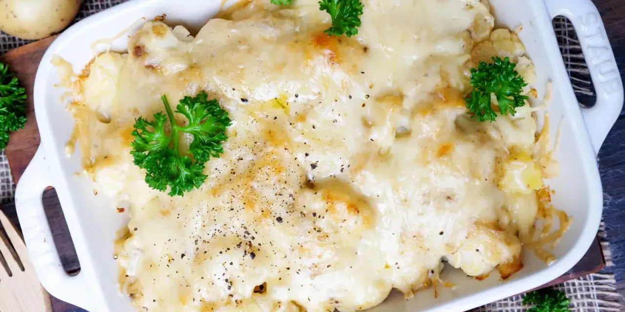 Herzhafter Blumenkohl Auflauf mit geschmolzenem Käse und frischer Petersilie, garniert mit Pfeffer.