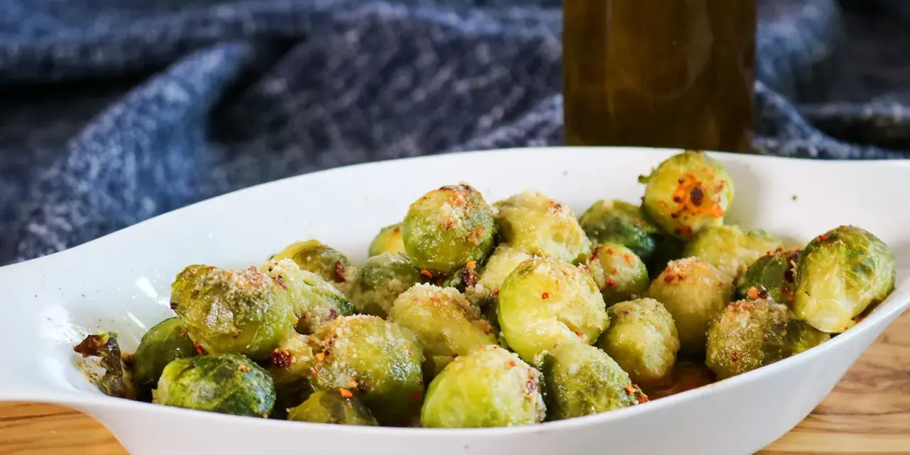 Ein weißes Ovalschälchen gefüllt mit knusprigem Rosenkohl, bestreut mit Parmesan und Chili-Flocken.